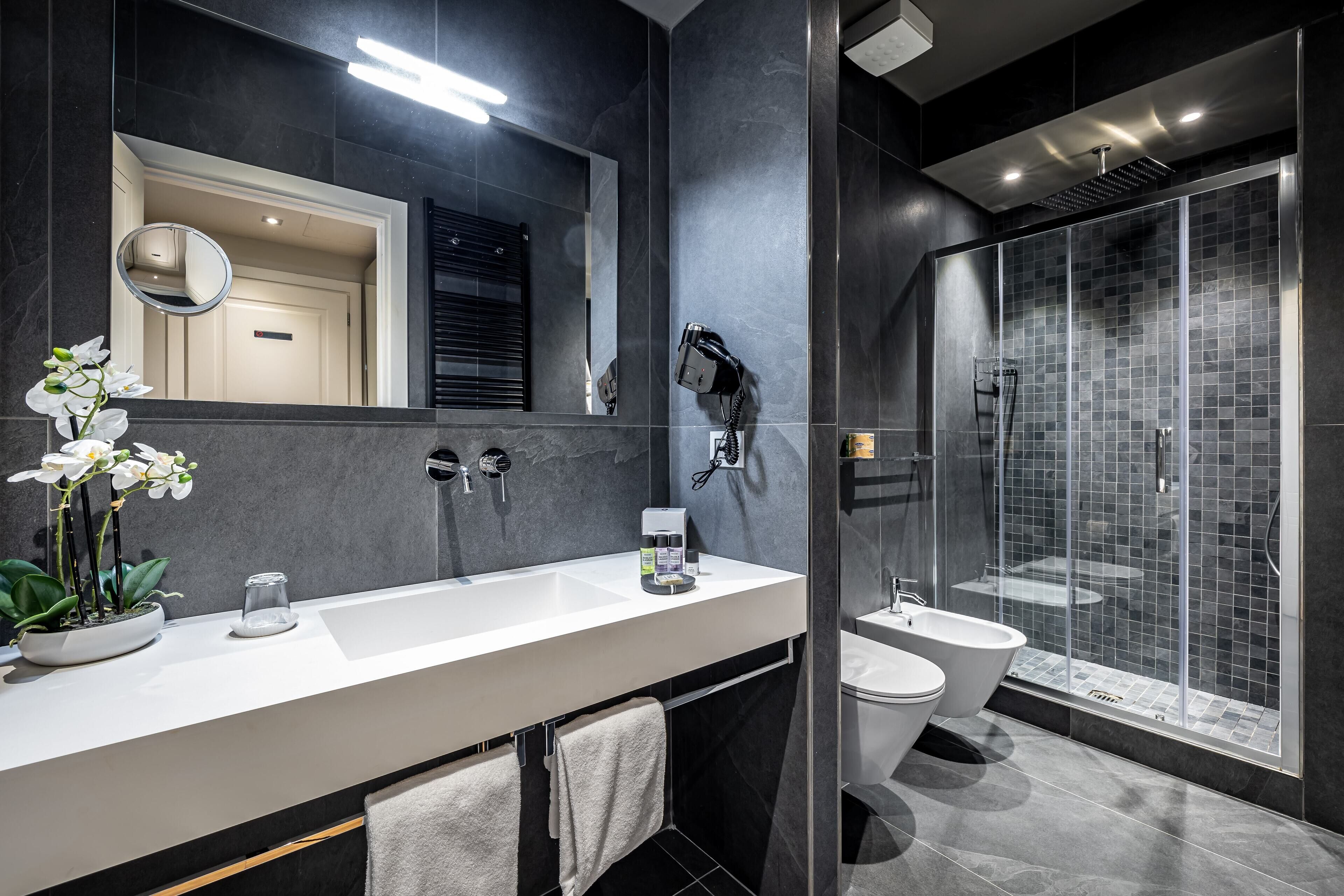 A modern bathroom with a large mirror, a sink, a toilet, and a glass-enclosed shower.