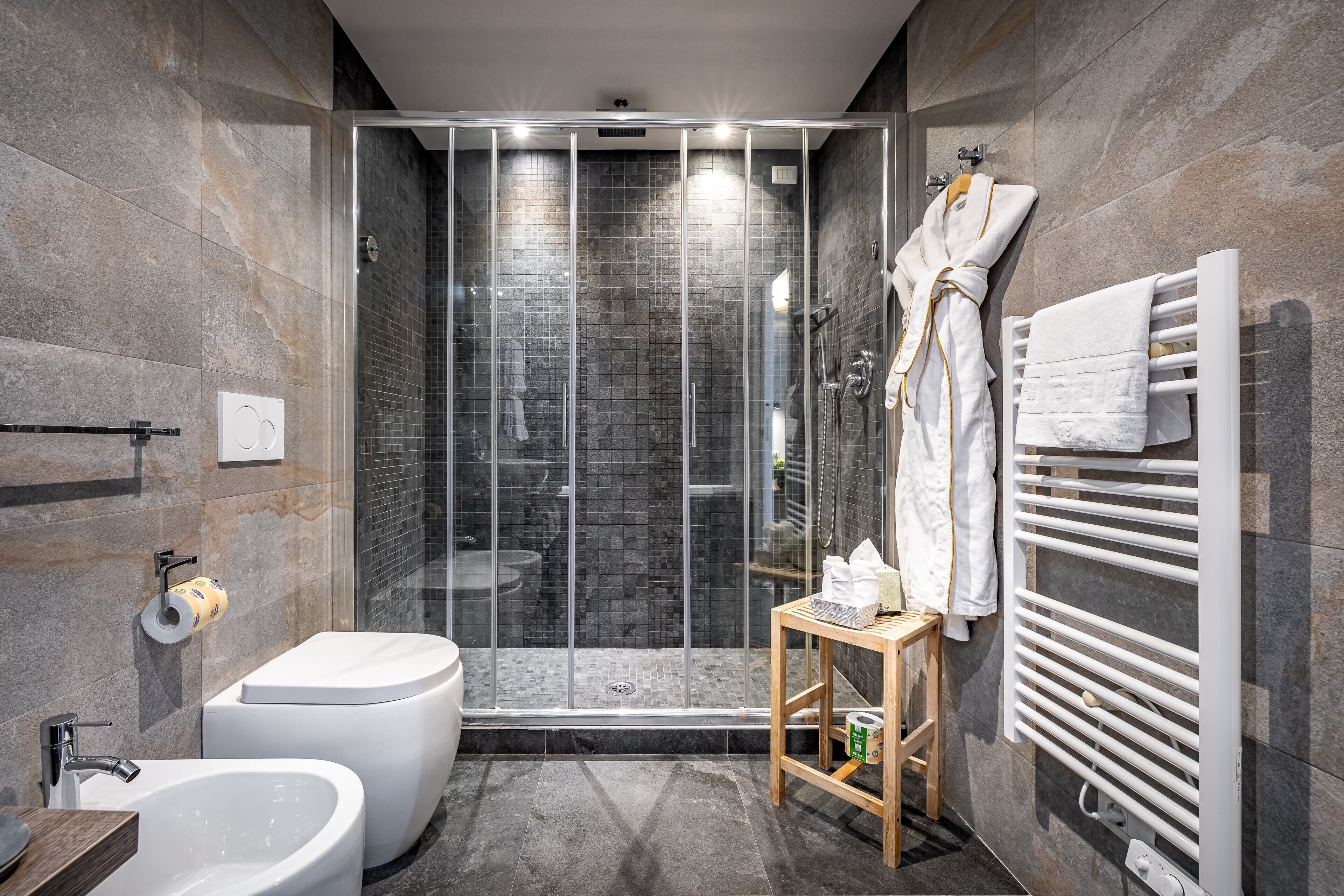 A modern bathroom with a glass-enclosed shower, a standalone bathtub, and a towel rack with towels.