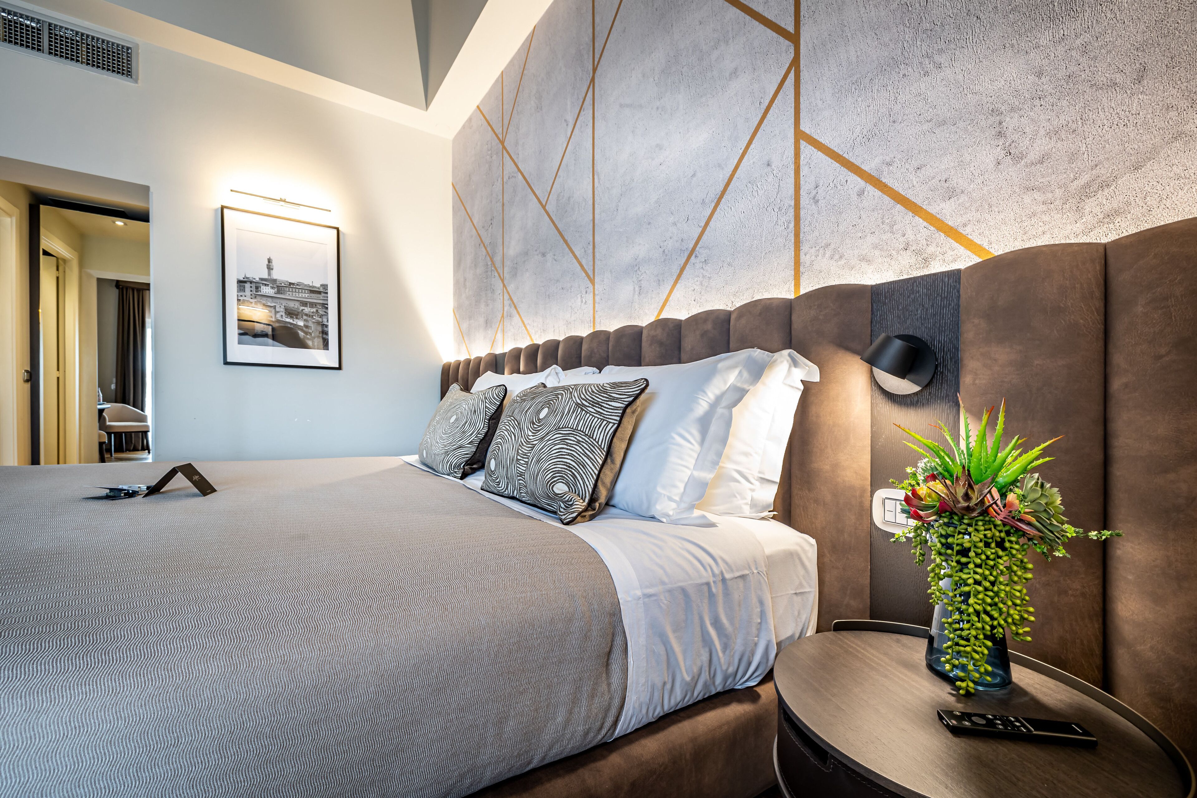 Una moderna camera d'hotel con un letto grande, un comodino con un telecomando e una lampada a parete.