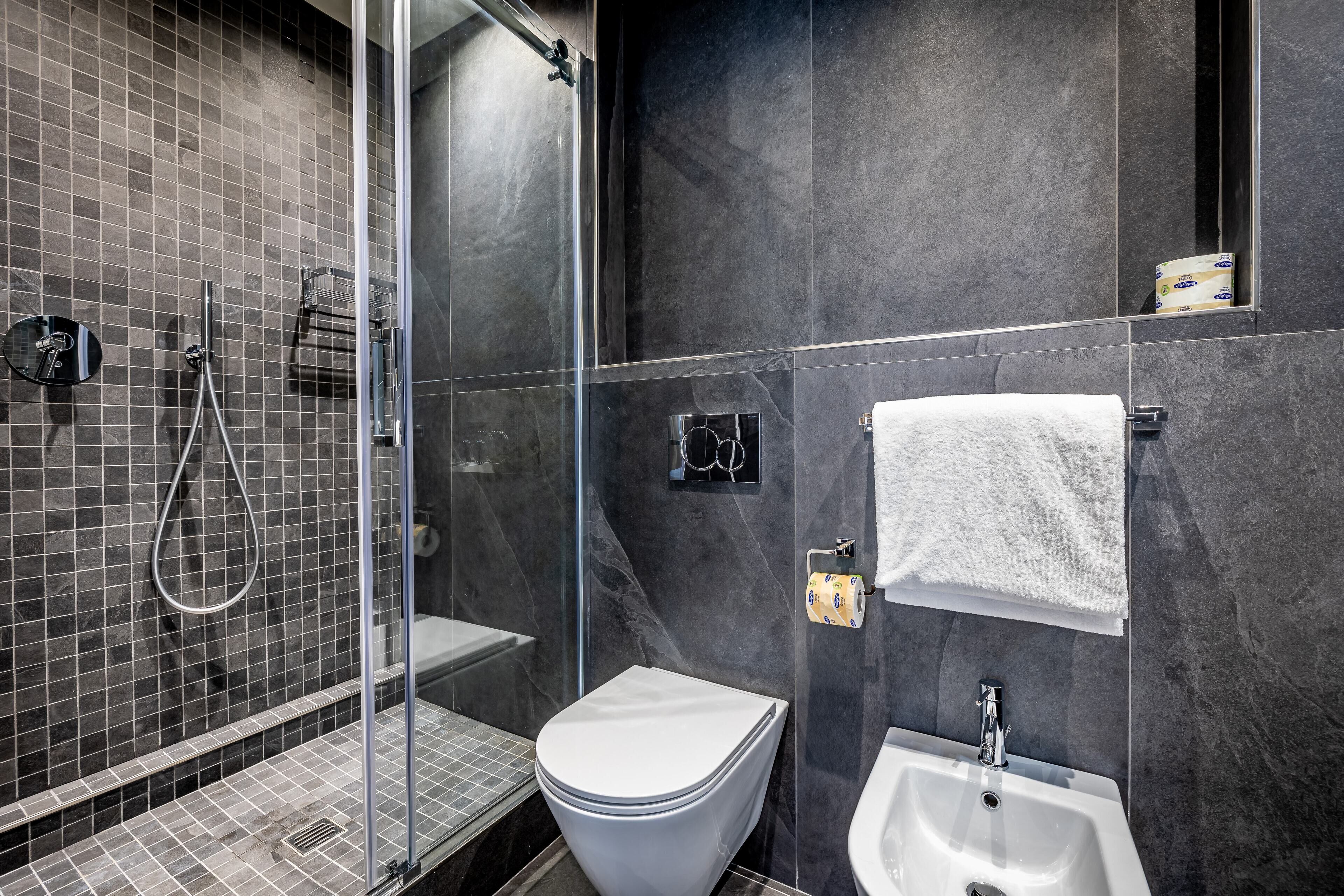 Un baño moderno con cabina de ducha de vidrio, inodoro blanco, lavamanos y toallero.