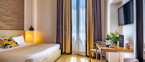 Une chambre d’hôtel avec un lit, un bureau, une chaise, une télévision et une fenêtre avec des rideaux.