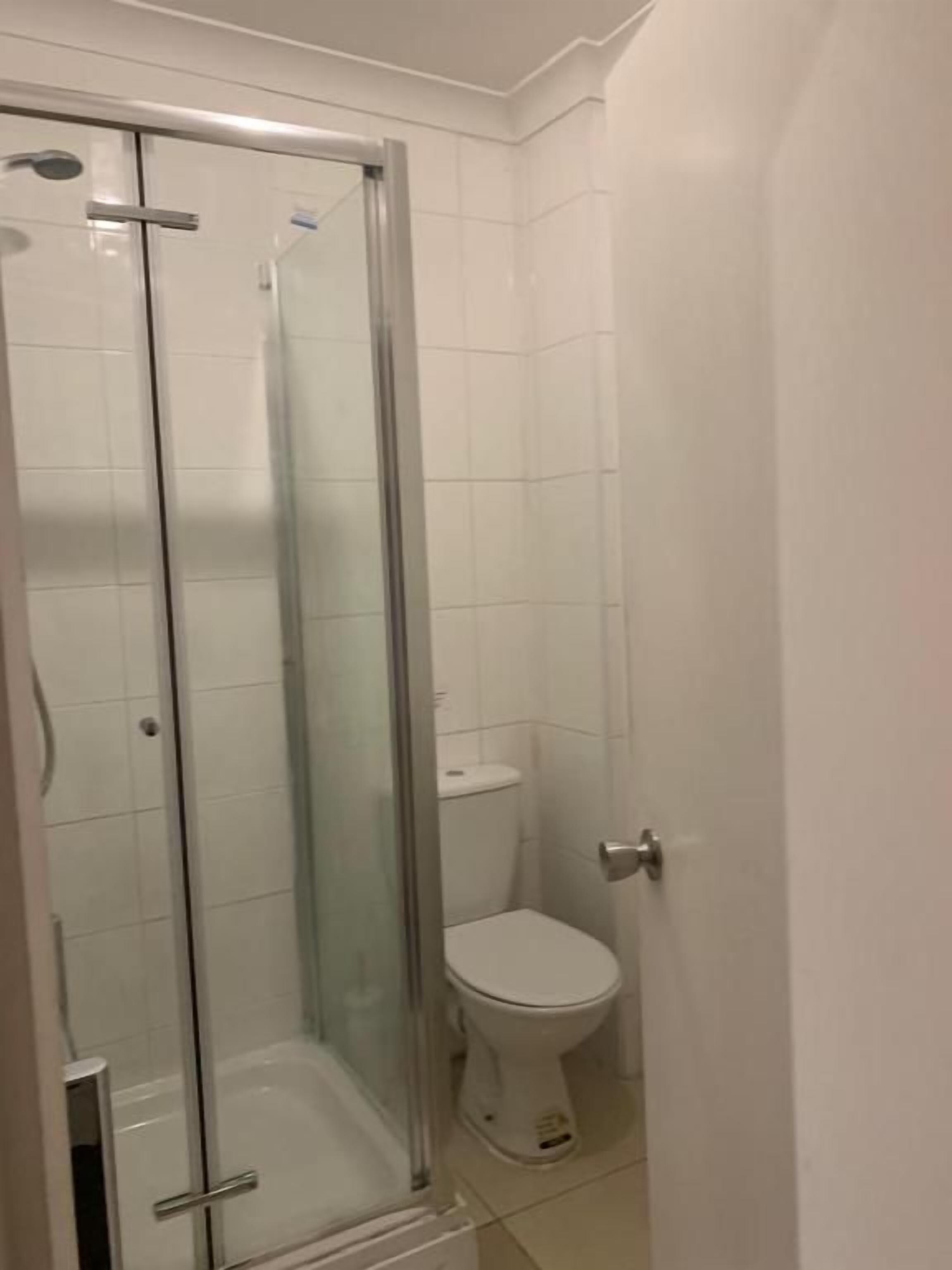 Une salle de bain avec une douche à parois de verre, des toilettes et un sol carrelé de couleur blanche.