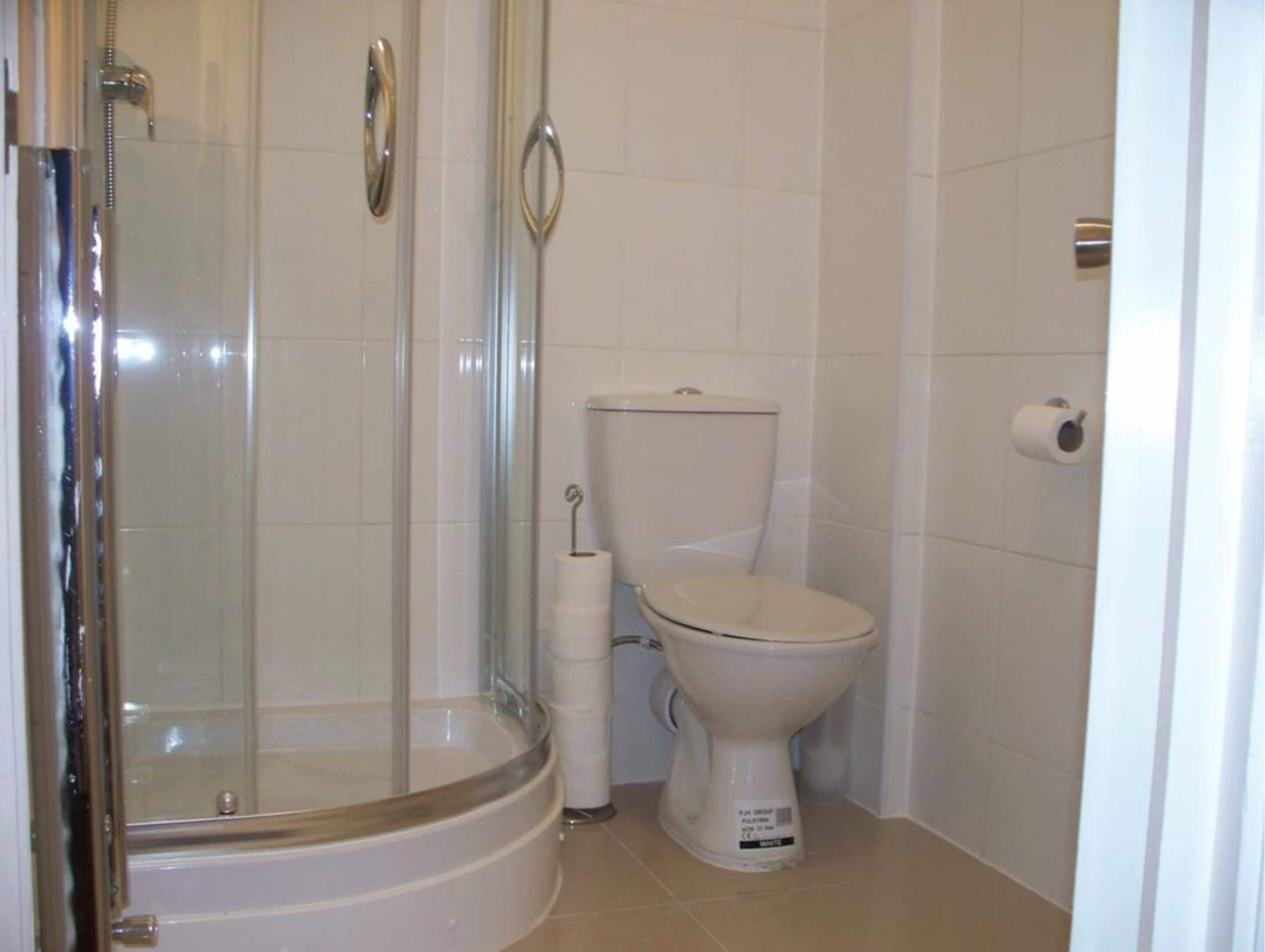 Un baño con ducha de vidrio, inodoro y un rollo de papel higiénico en la pared.