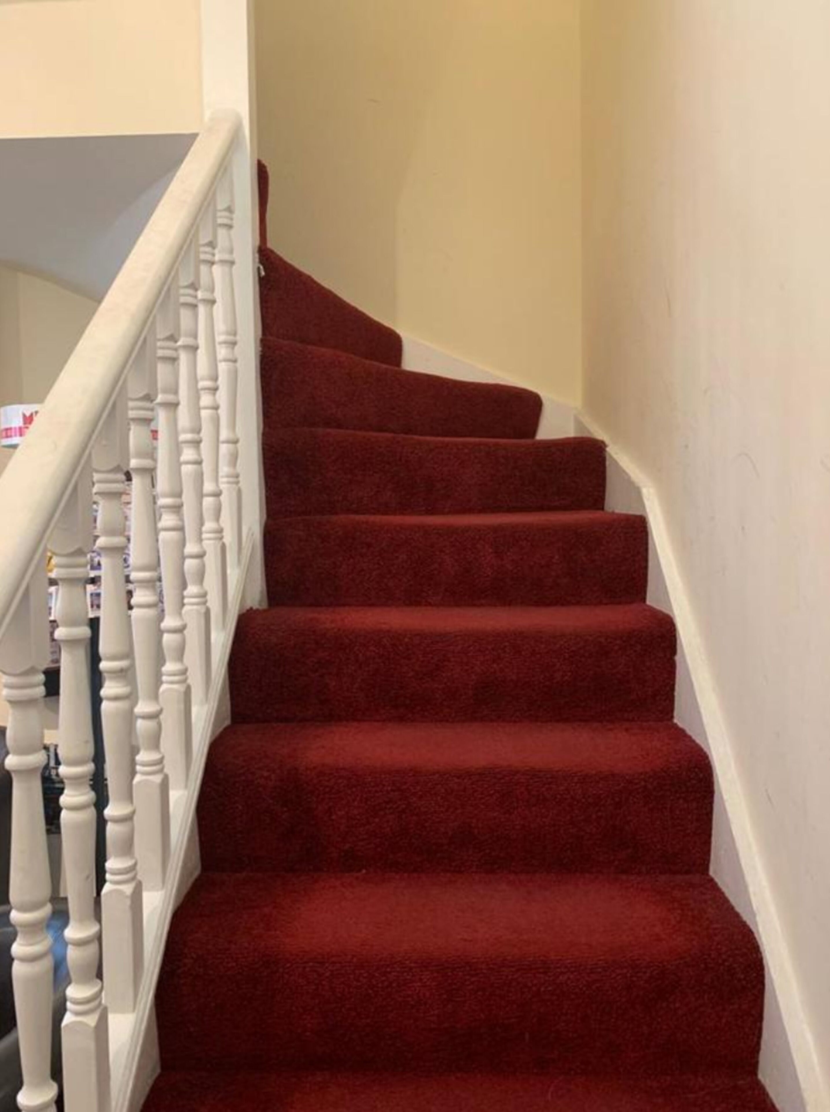 A staircase with red carpeted steps and white balusters.