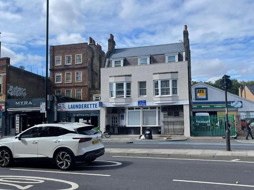 A street view with a white car parked in front of a building with a sign that reads 'LAUNDERETTE.'