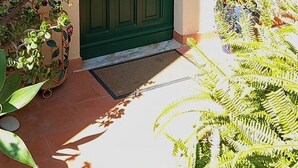 A green door with hanging flower pots, a wall with various decorations, and a potted plant to the left. - B&B Rosangela (Taormina)