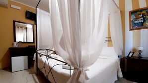 A bedroom with a bed, a bedside table, a small desk, a chair, a television, and a painting on the wall. - B&B Rosangela (Taormina)