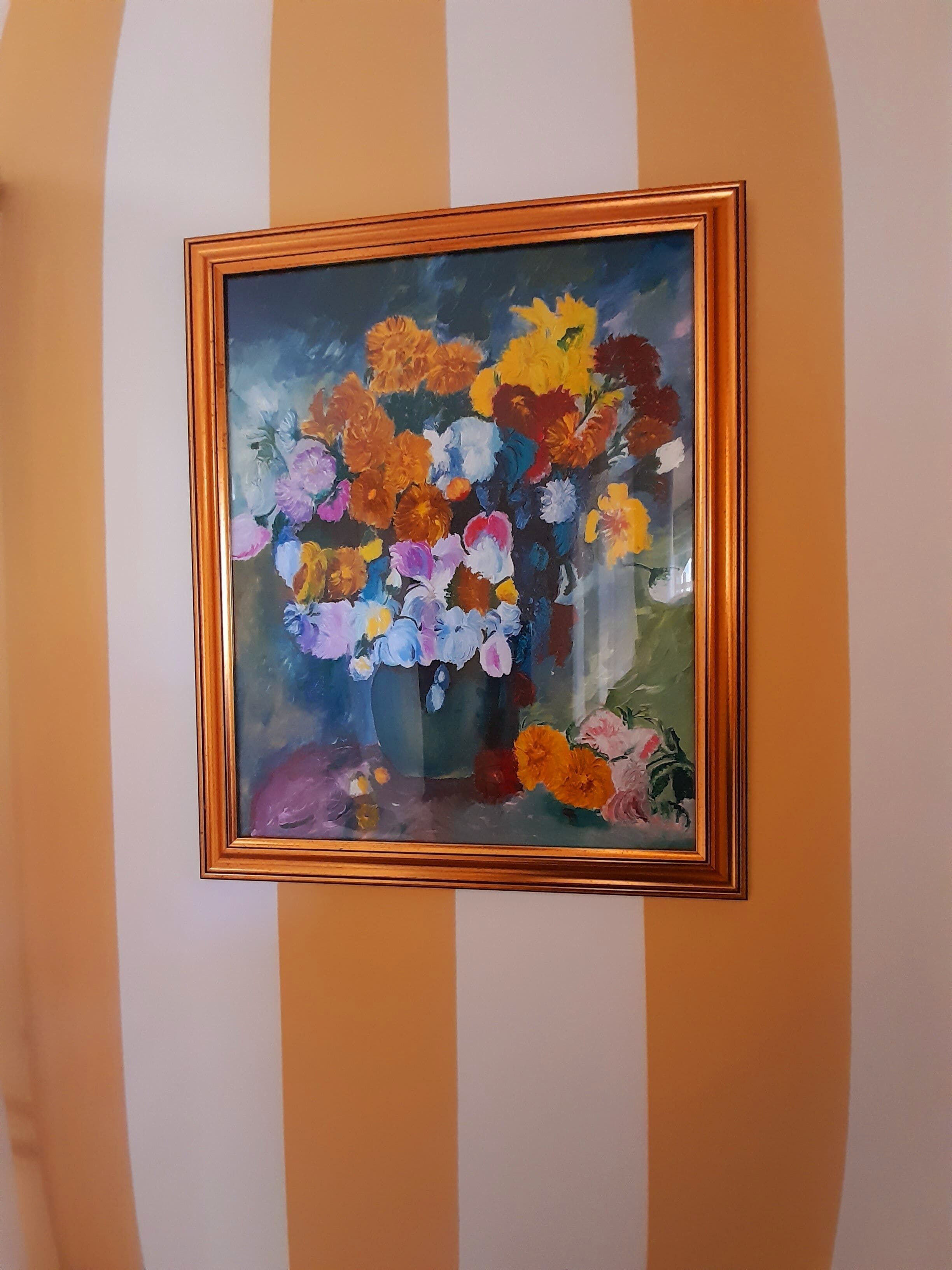 A framed painting of a bouquet of flowers on a wall with vertical stripes.