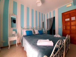 A bedroom with a bed, a nightstand, a mirror, a door, and a wall with vertical stripes.