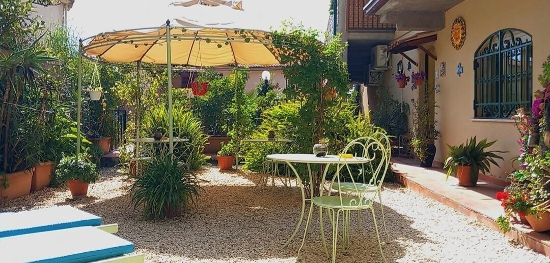 A patio area with a table and chairs, surrounded by potted plants and a pergola providing shade.
