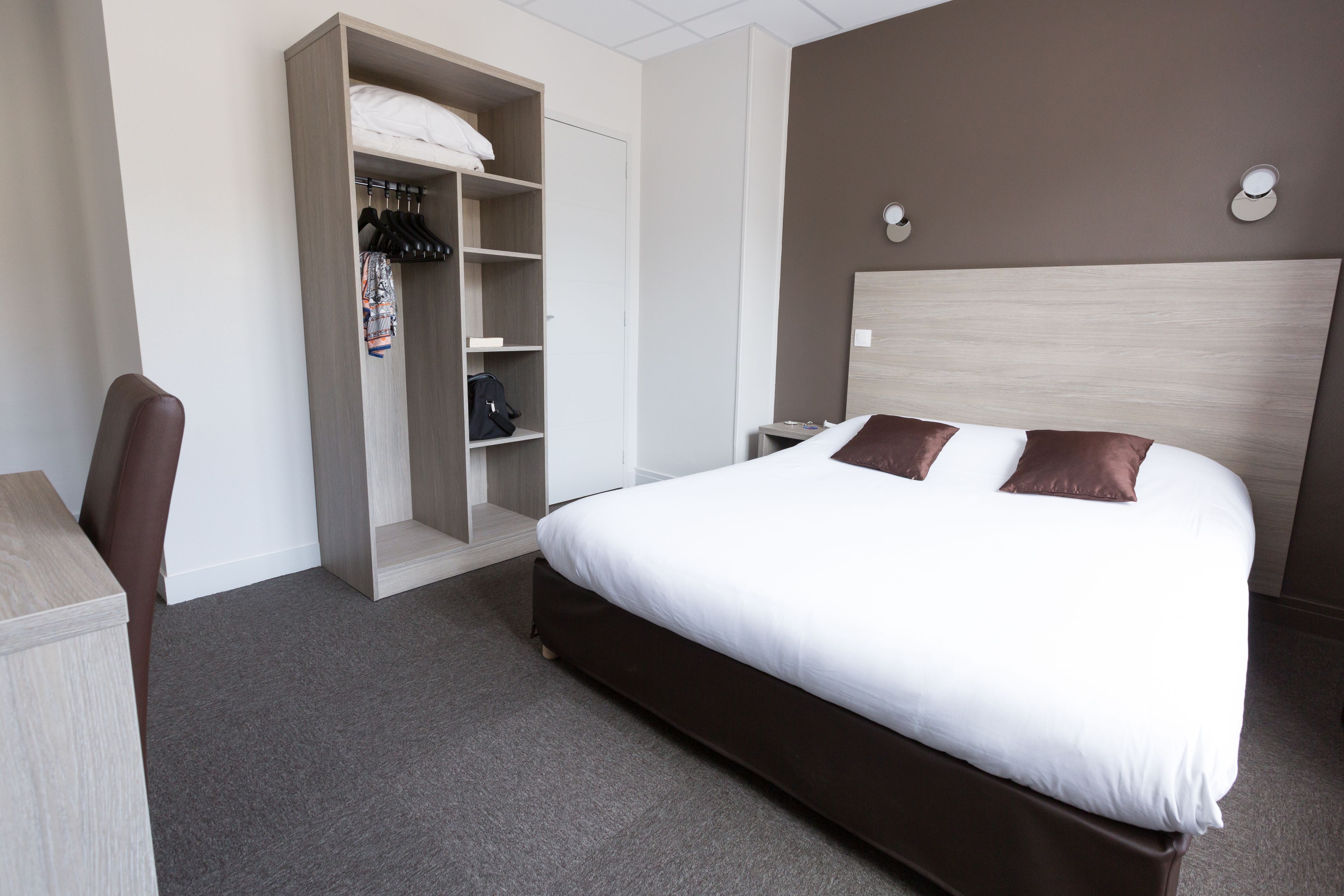 A hotel room with a bed, a wardrobe, a desk, and a chair.