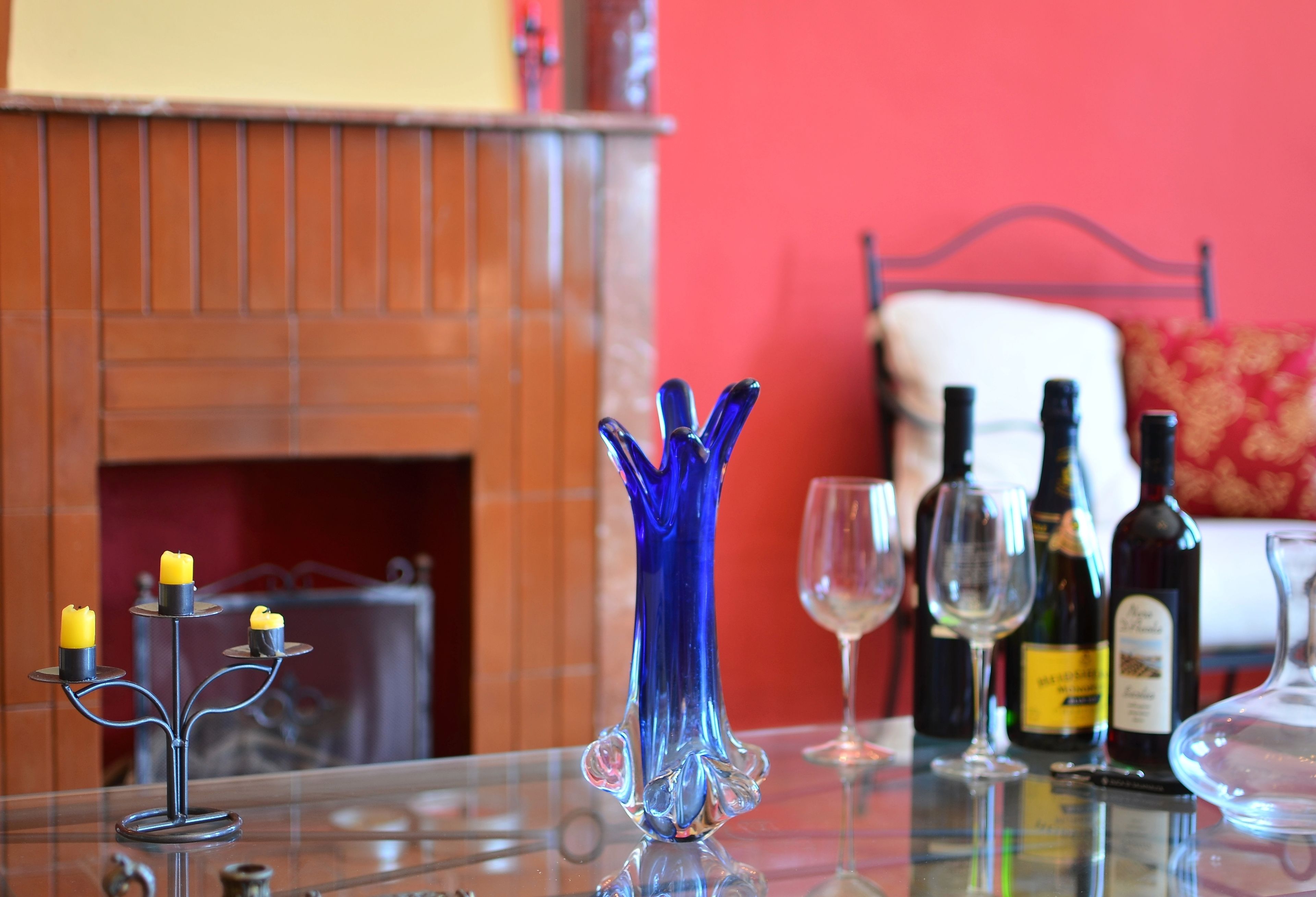 Un tavolo in vetro con un vaso blu, candele, bicchieri da vino e bottiglie.