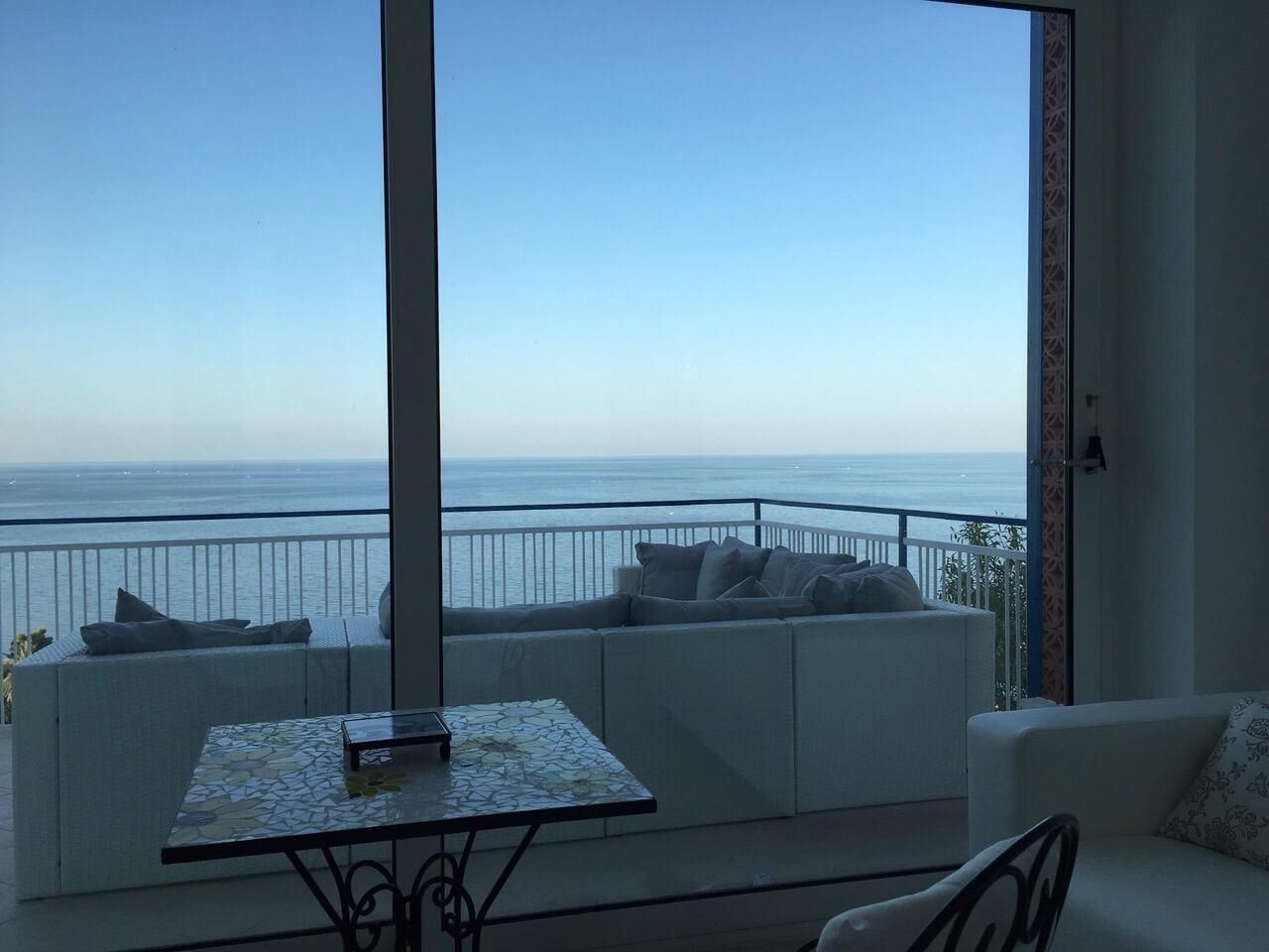 Un balcone con un divano bianco e un tavolino, affacciato su una limpida vista del mare.