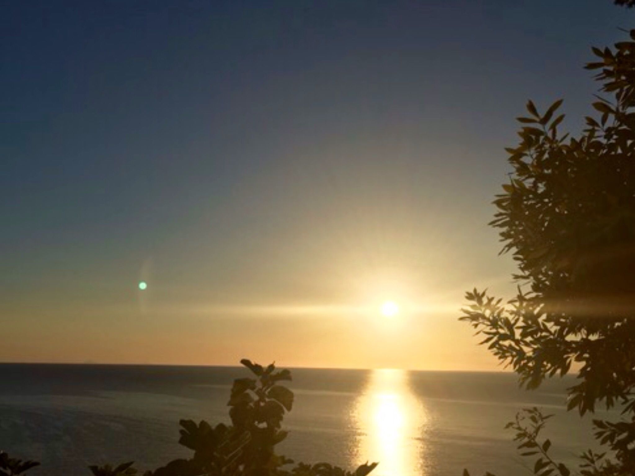 Tramonto sull'oceano con sagome di vegetazione sullo sfondo.