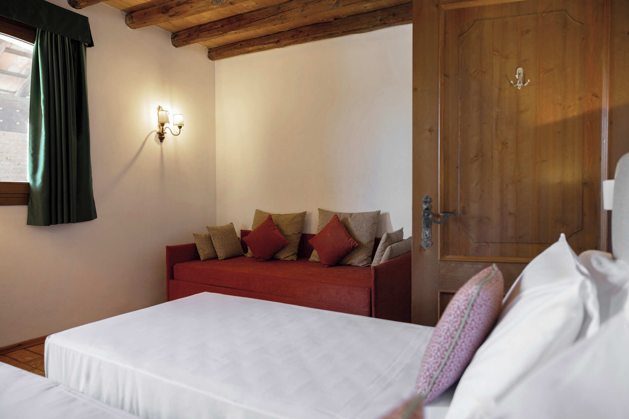A bedroom with a bed, a red sofa, a wall-mounted light fixture, and a wooden door.