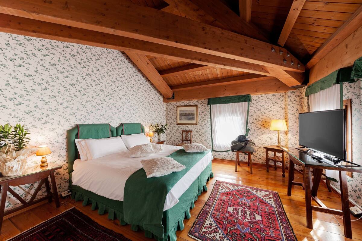 A bedroom with a large bed, wooden beams, a television, and a desk.