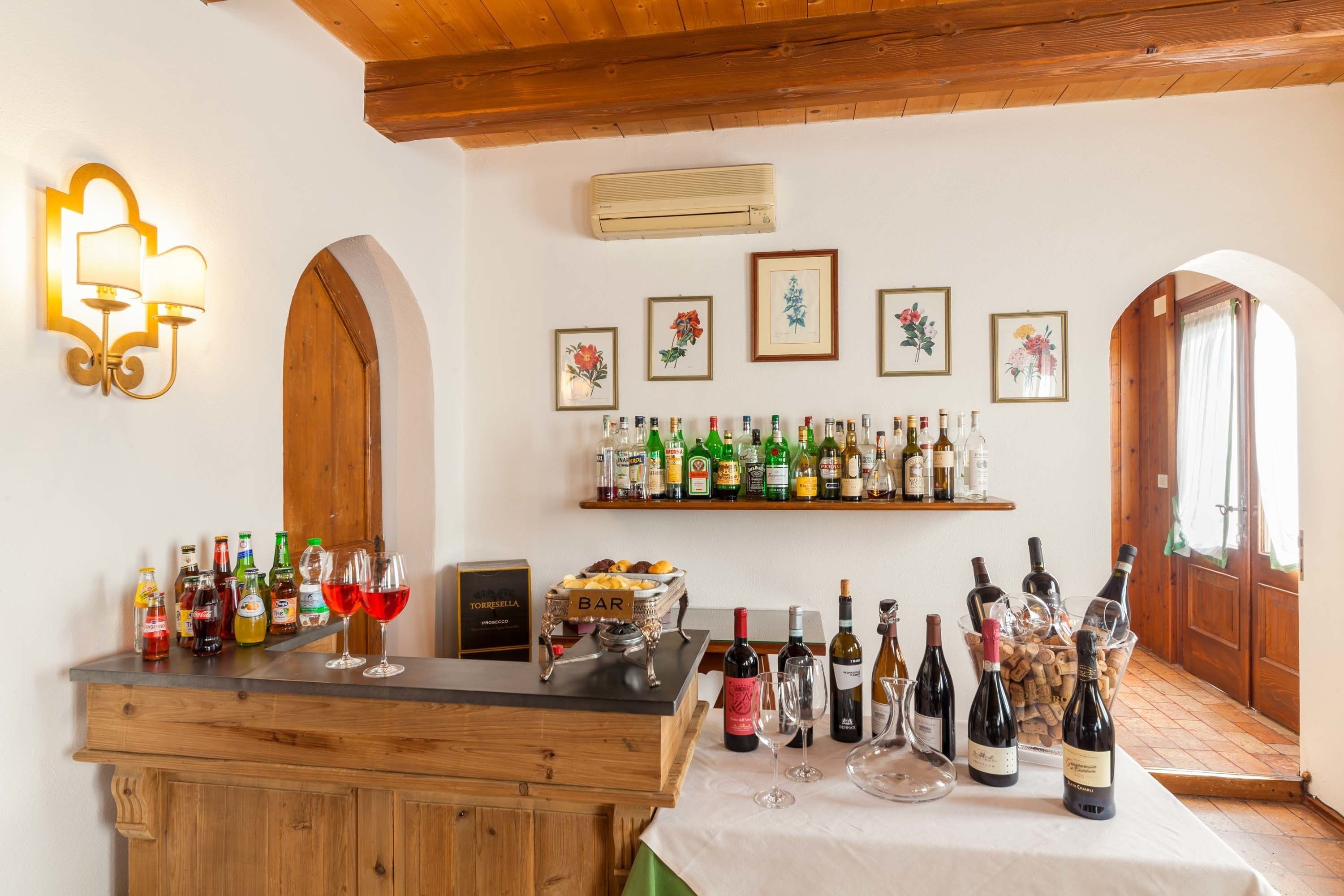 Una zona de bar con mostrador de madera, estanterías con botellas y cuadros con motivos florales en la pared.