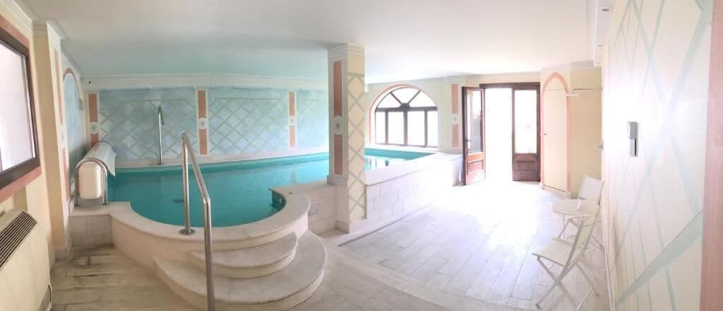 A swimming pool with steps leading into it, a door leading to another room, and a window with a view.