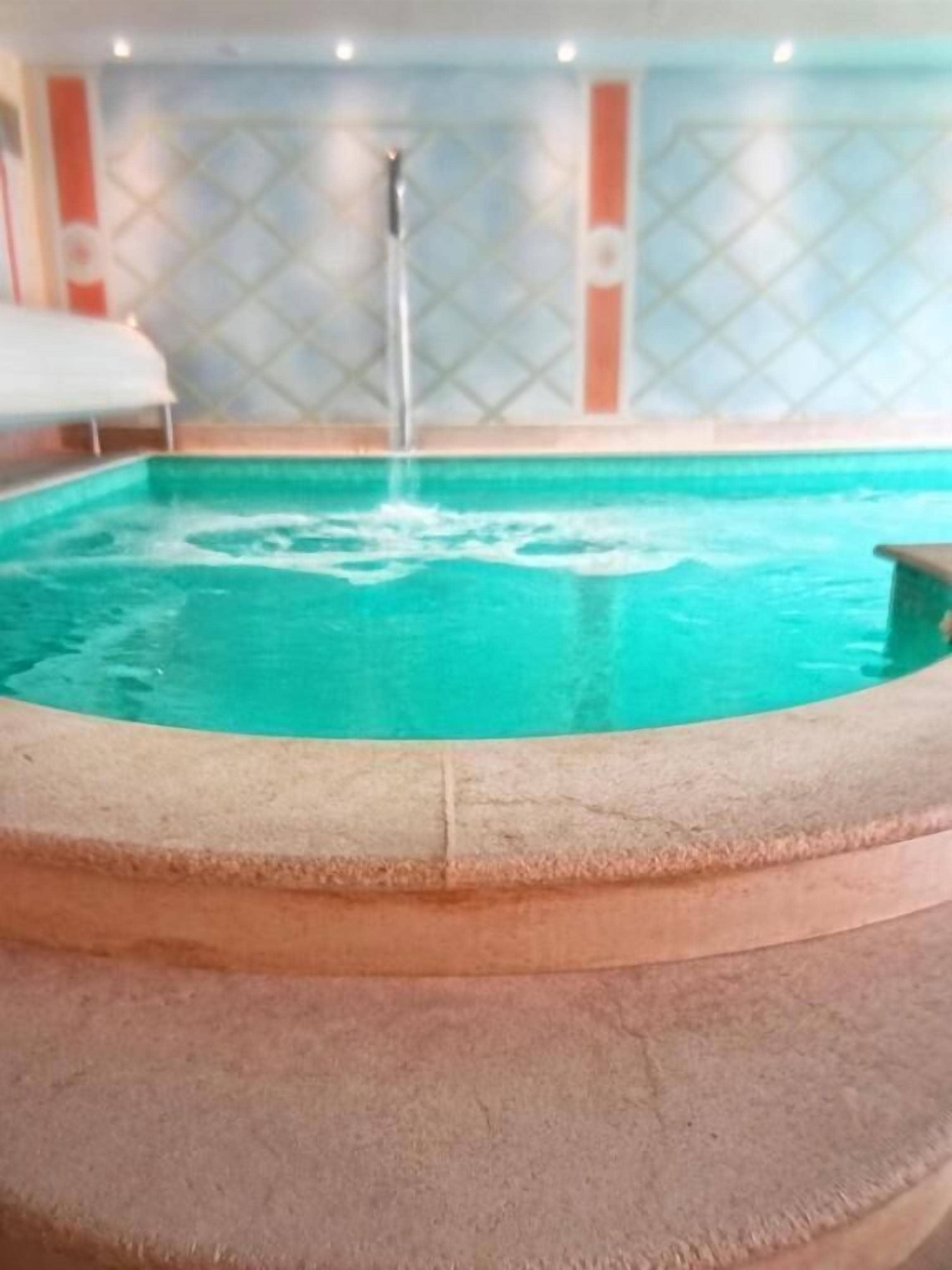 Een ronde zwembad met een waterfontein, omringd door een beige rand.