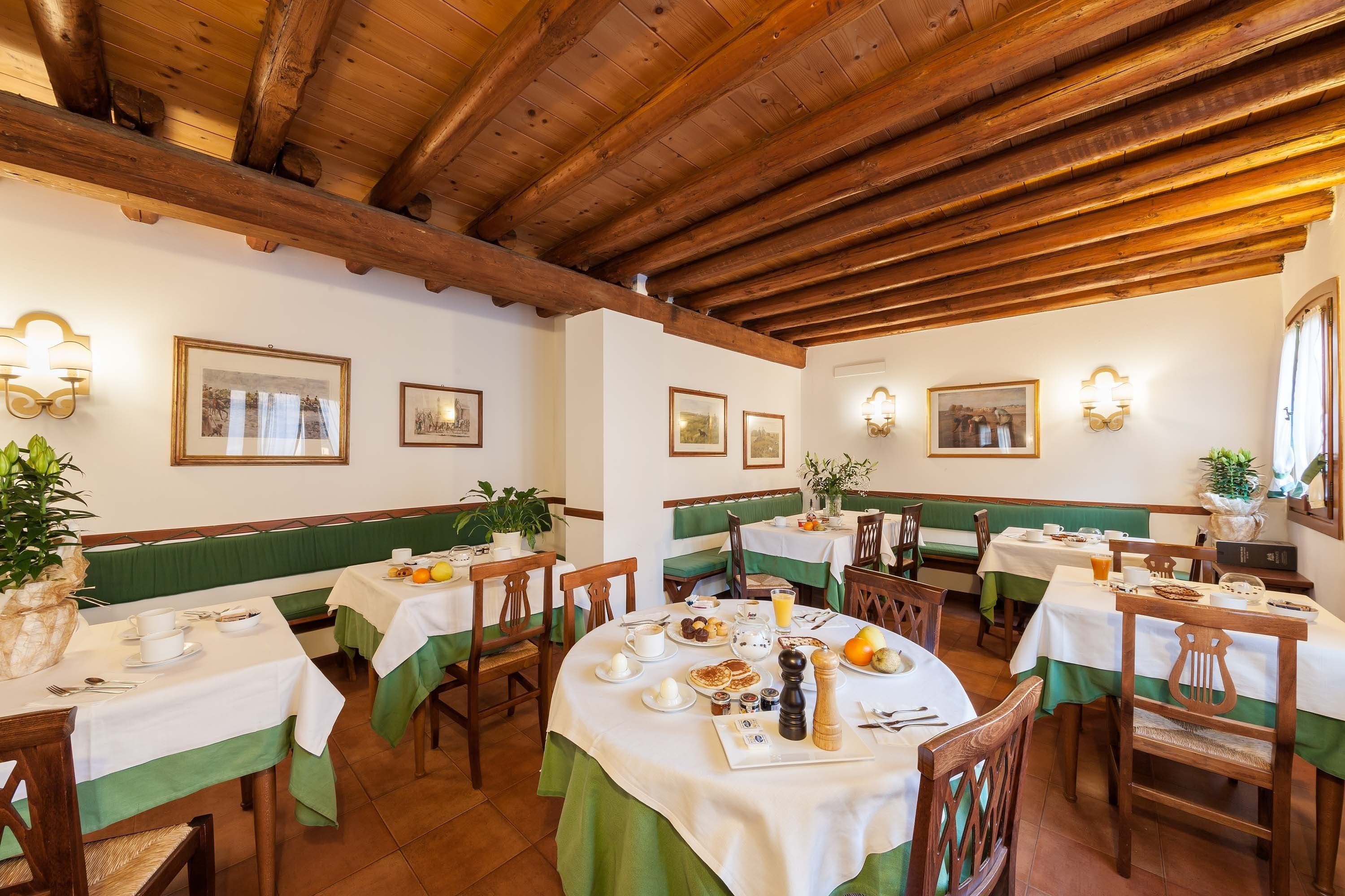 A restaurant with wooden beams, green cushioned benches, and tables set for breakfast.