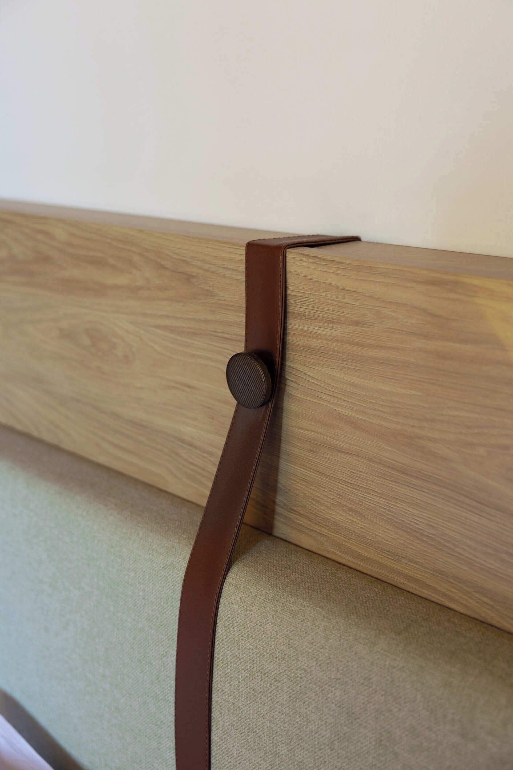 A corner of a room with a wooden headboard and a brown leather strap.