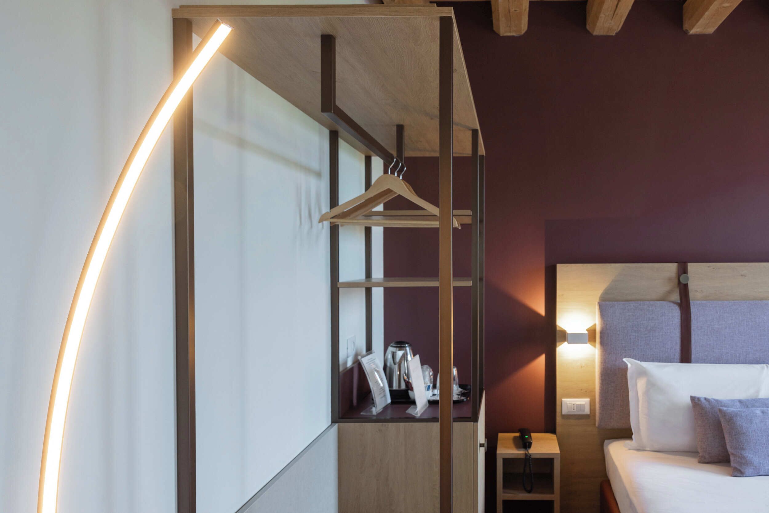 A hotel room with a bed, bedside table, and a wardrobe with a hanging rack.