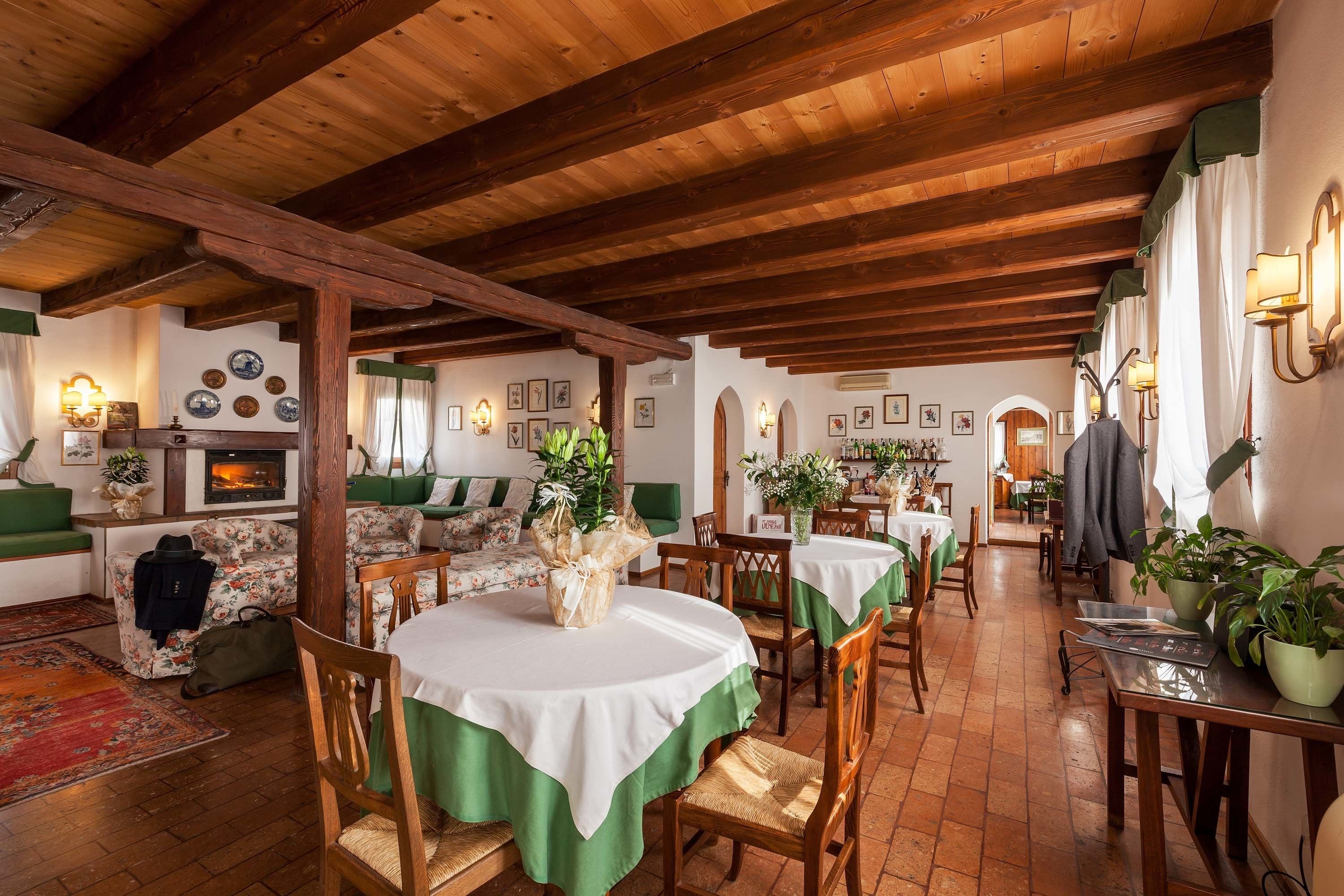 Un comedor rústico con vigas de madera, manteles blancos y verdes, y sillas de madera.