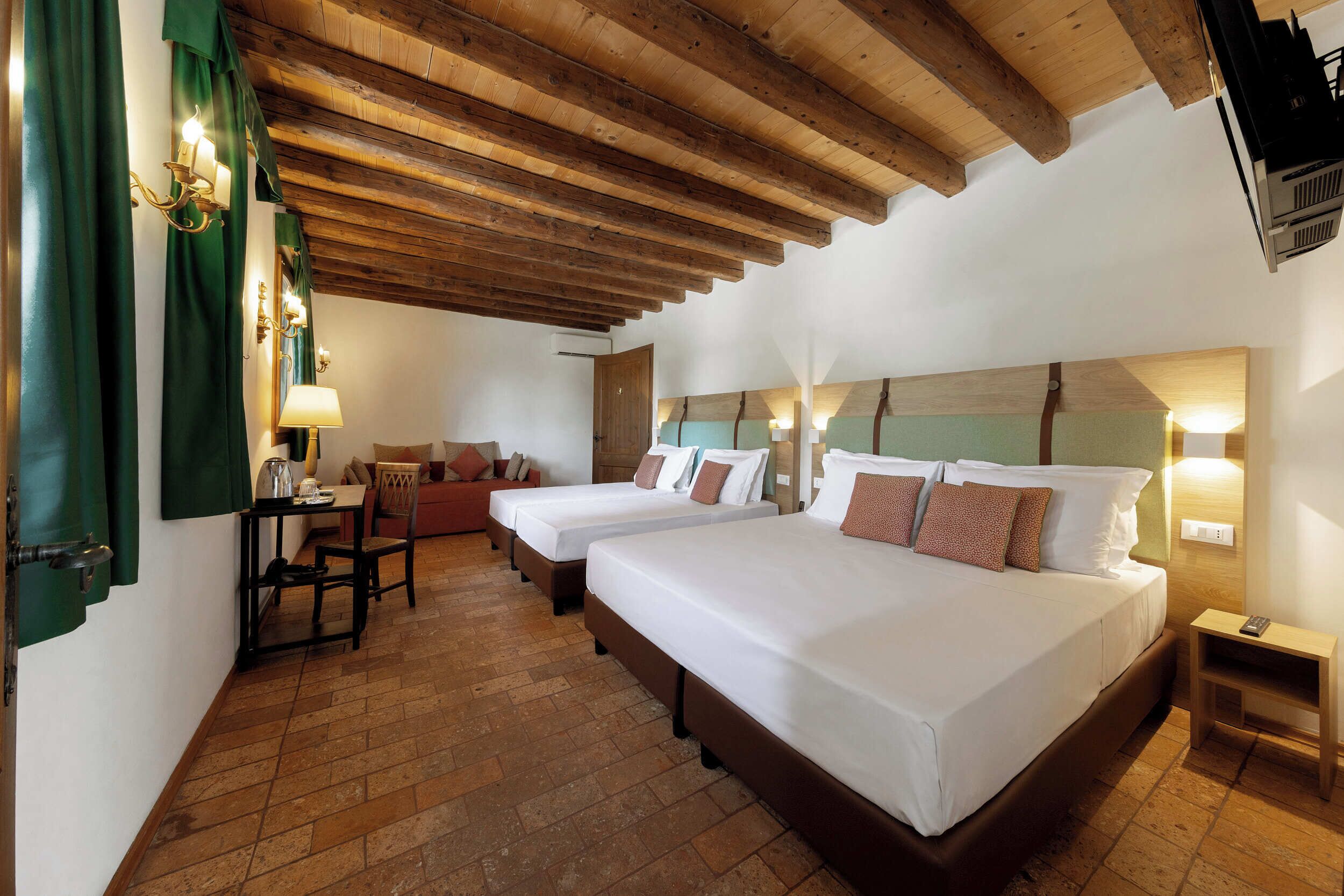 A hotel room with two beds, a wooden ceiling, a small table with a lamp, and a chair.