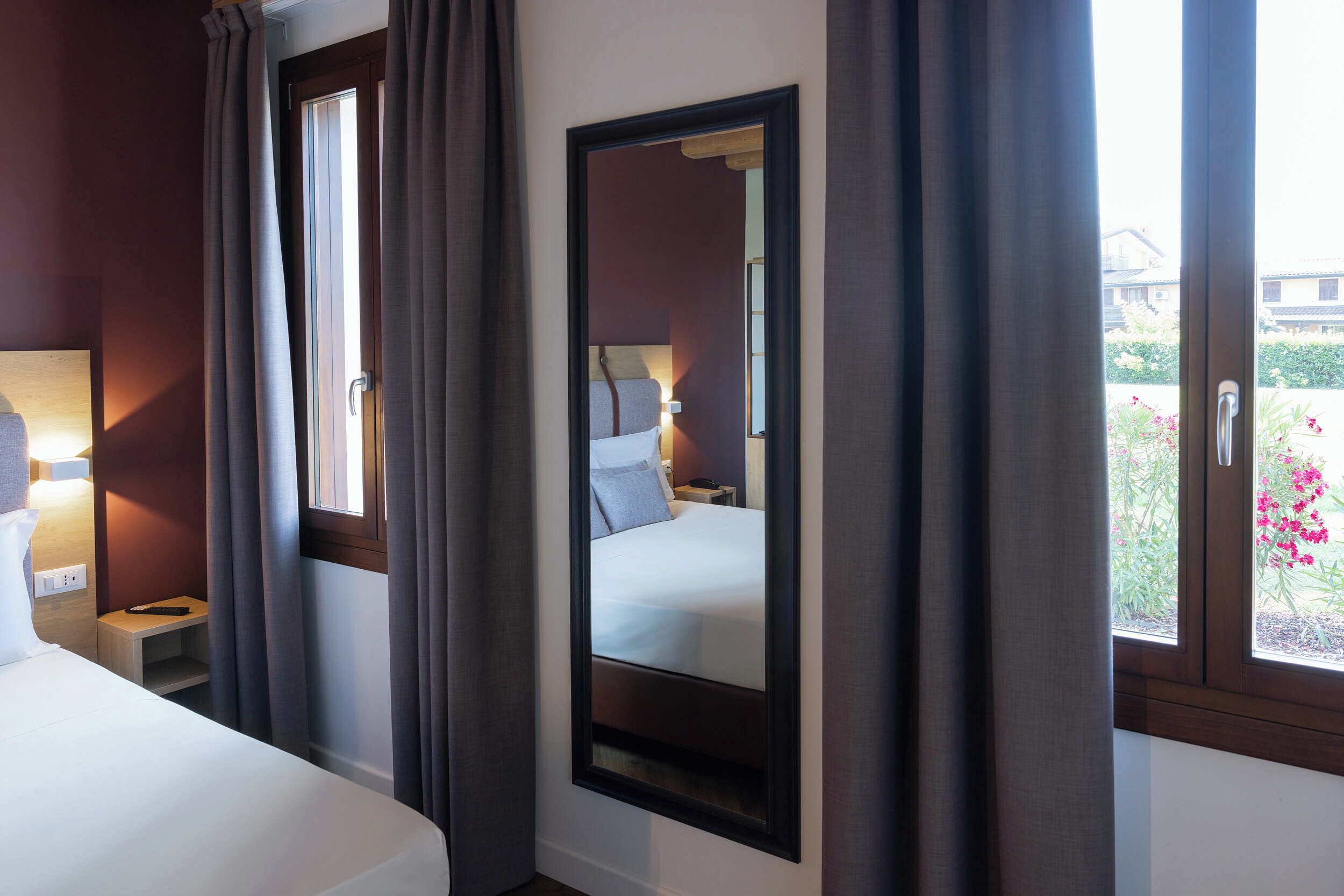 Een hotelkamer met een bed, nachtkastje, lamp en een raam met gordijnen.