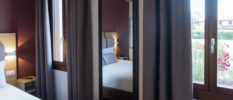 Une chambre d’hôtel avec un lit, une table de chevet, une lampe et une fenêtre avec des rideaux.