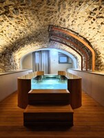A stone-walled room with a wooden bathtub and a window.