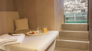 A room with a bed, a breakfast tray with fruit and juice, and a view of a stone wall outside.