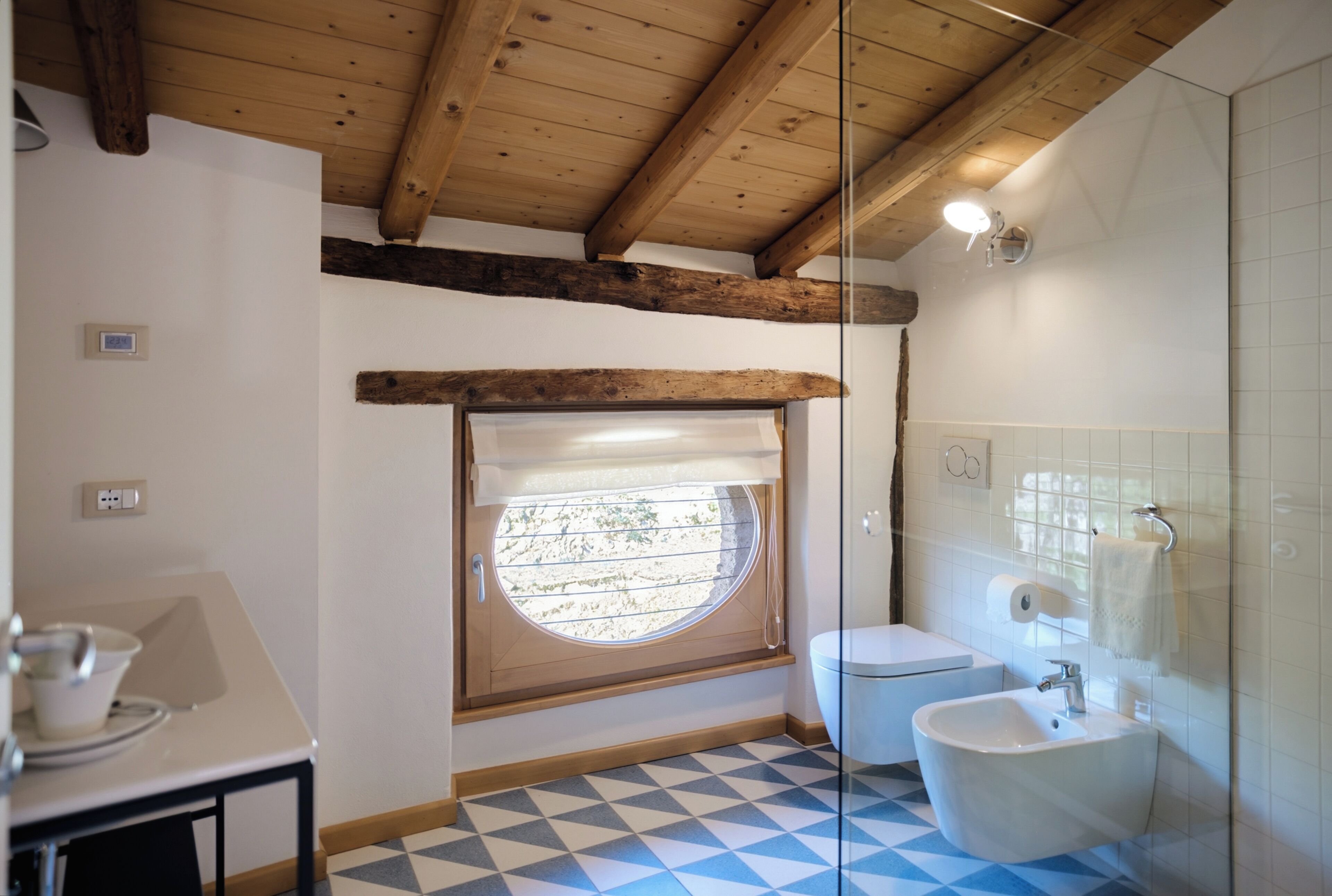 Une salle de bain avec un carrelage à motifs, des toilettes, un lavabo et une fenêtre donnant sur un paysage agréable.