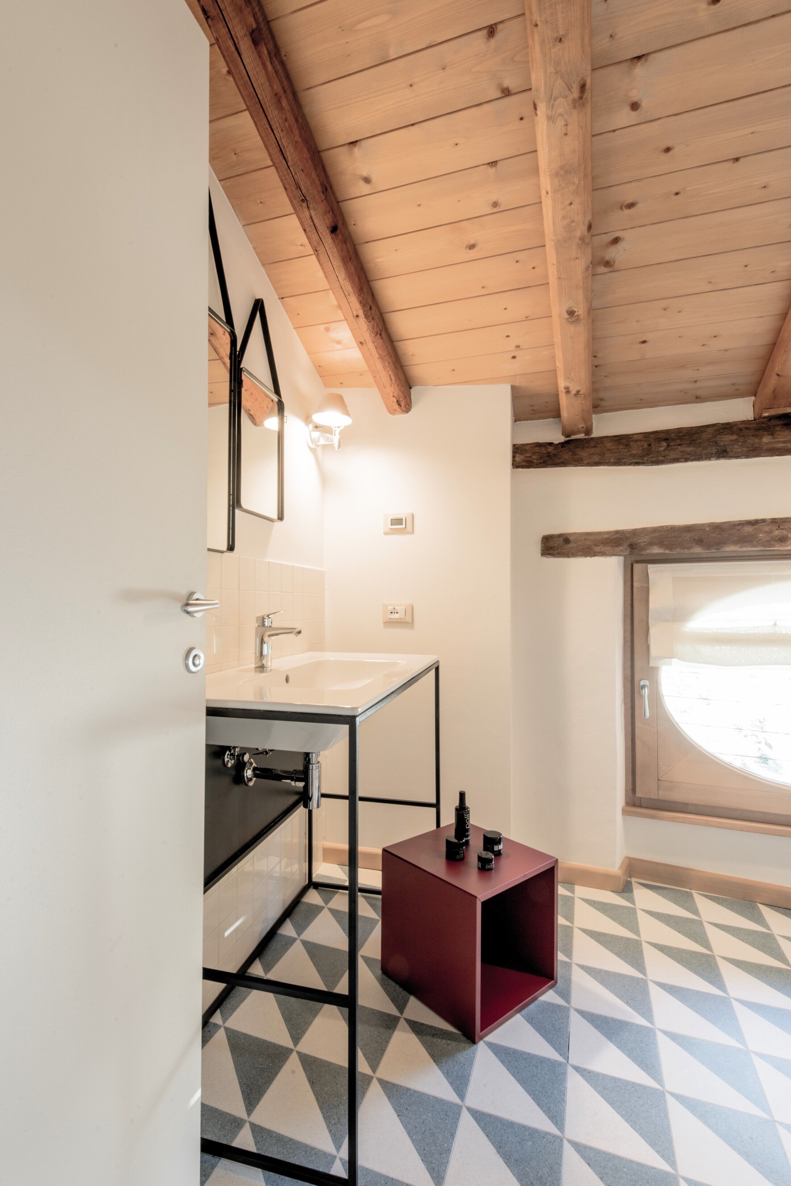 Un baño con techo de madera, un lavamanos blanco, un espejo y una ventana con vistas.