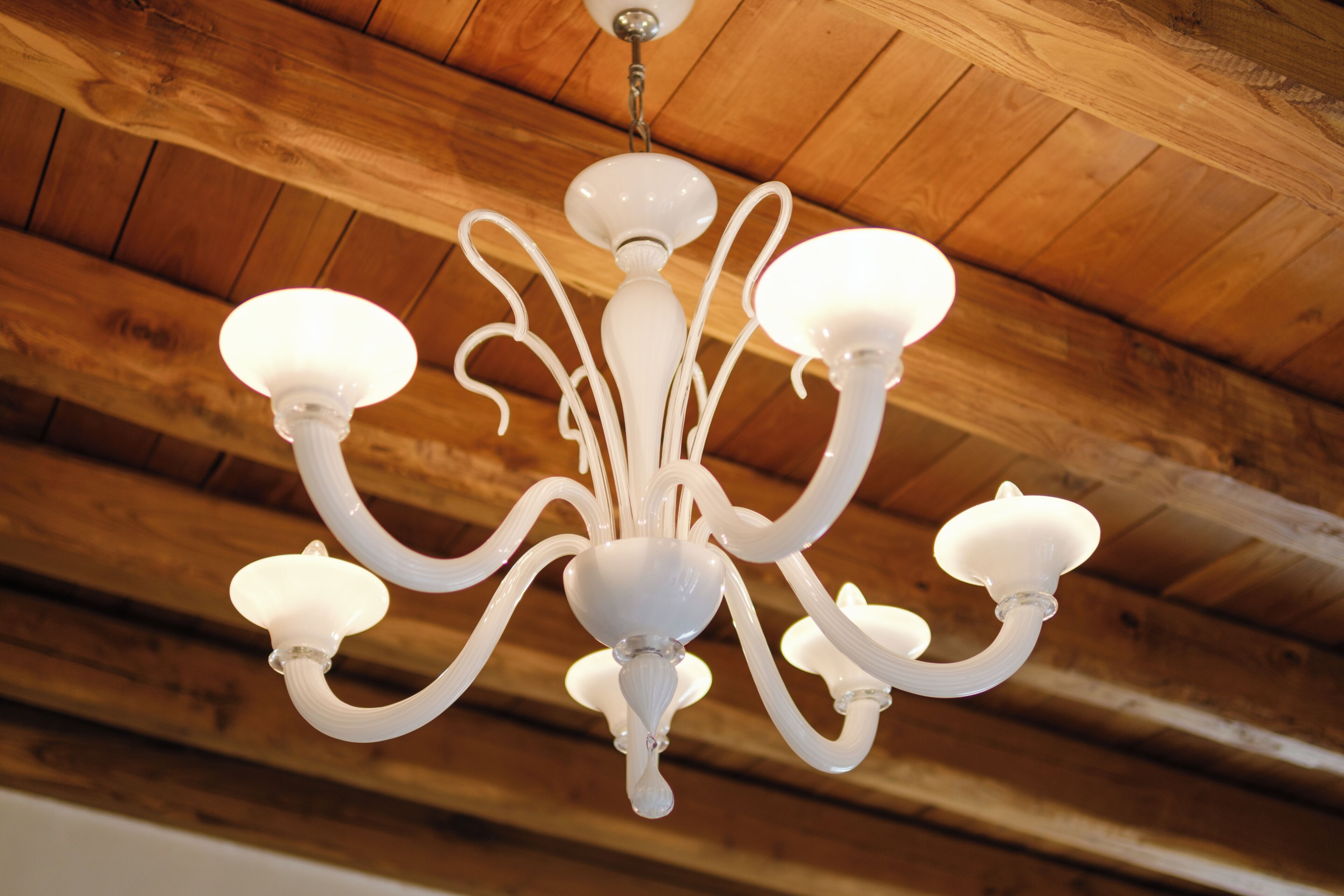 Un lustre à plusieurs bras et à plusieurs points lumineux, suspendu à un plafond en bois.