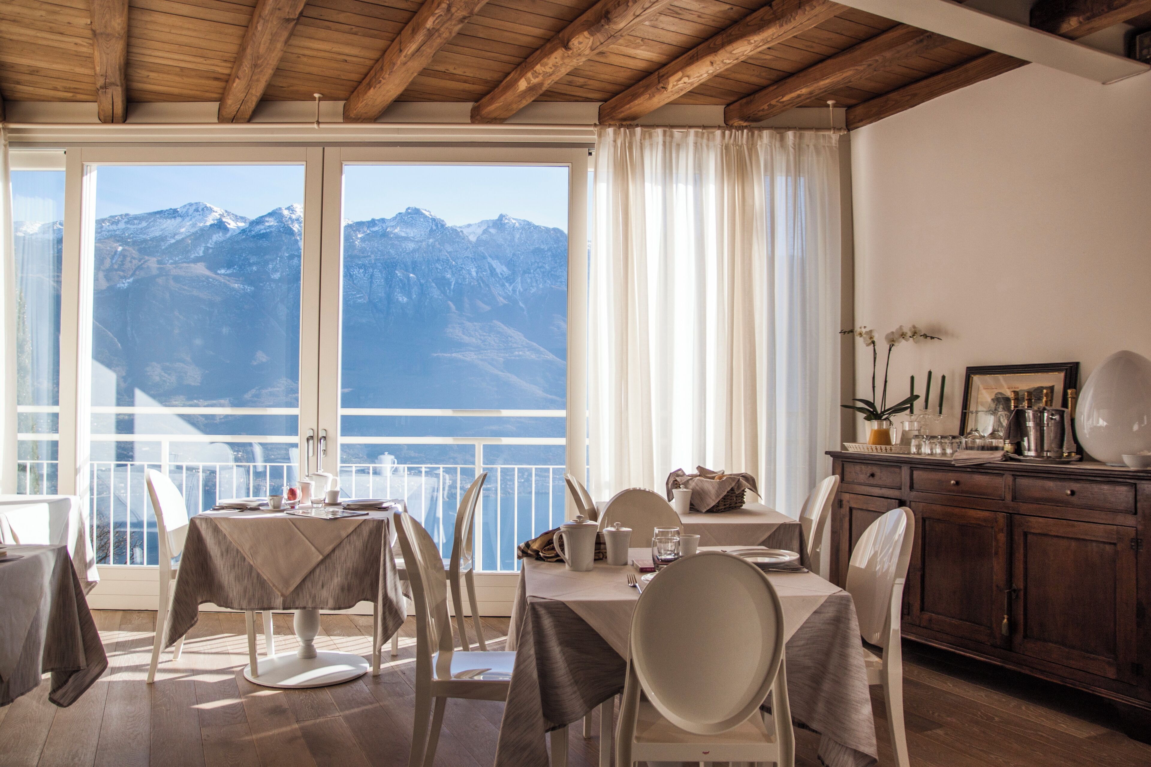 Un coin repas avec une table dressée pour deux personnes, un plafond en bois et une vue sur les montagnes à travers de grandes fenêtres.