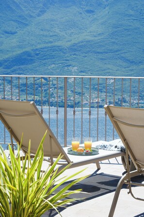 A balcony with two lounge chairs, a table with a tray of fruit and drinks, and a view of the sea. - Locanda Al Castelletto (Tremosine)