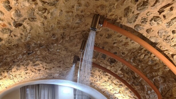 Un bain à remous entouré de murs en pierre, avec un banc en bois et une pomme de douche placée au-dessus.