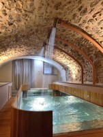 A stone-walled hot tub with a wooden bench and a showerhead above it.