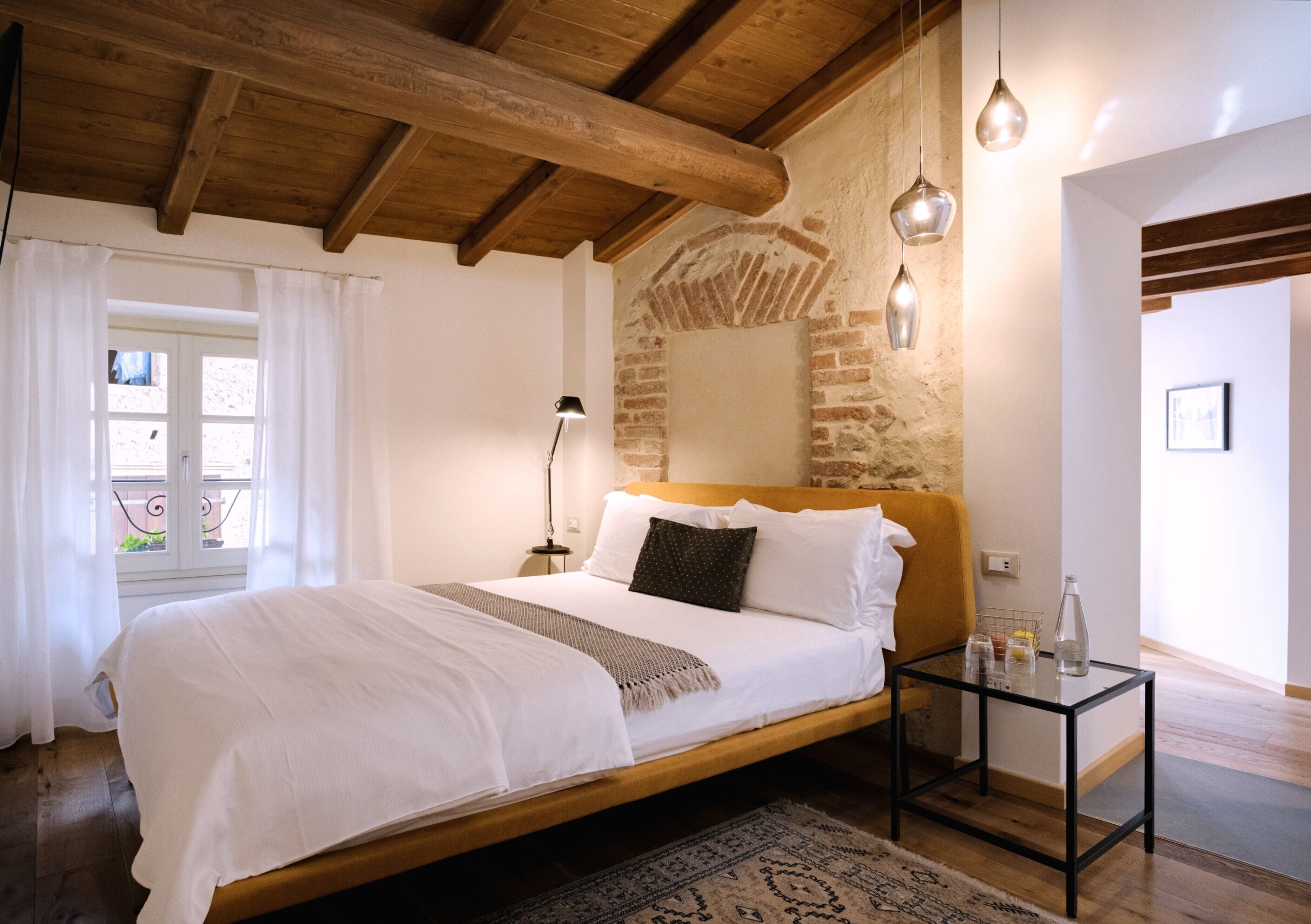 A bedroom with a wooden bed, a nightstand, a lamp, and a glass table with a bottle.