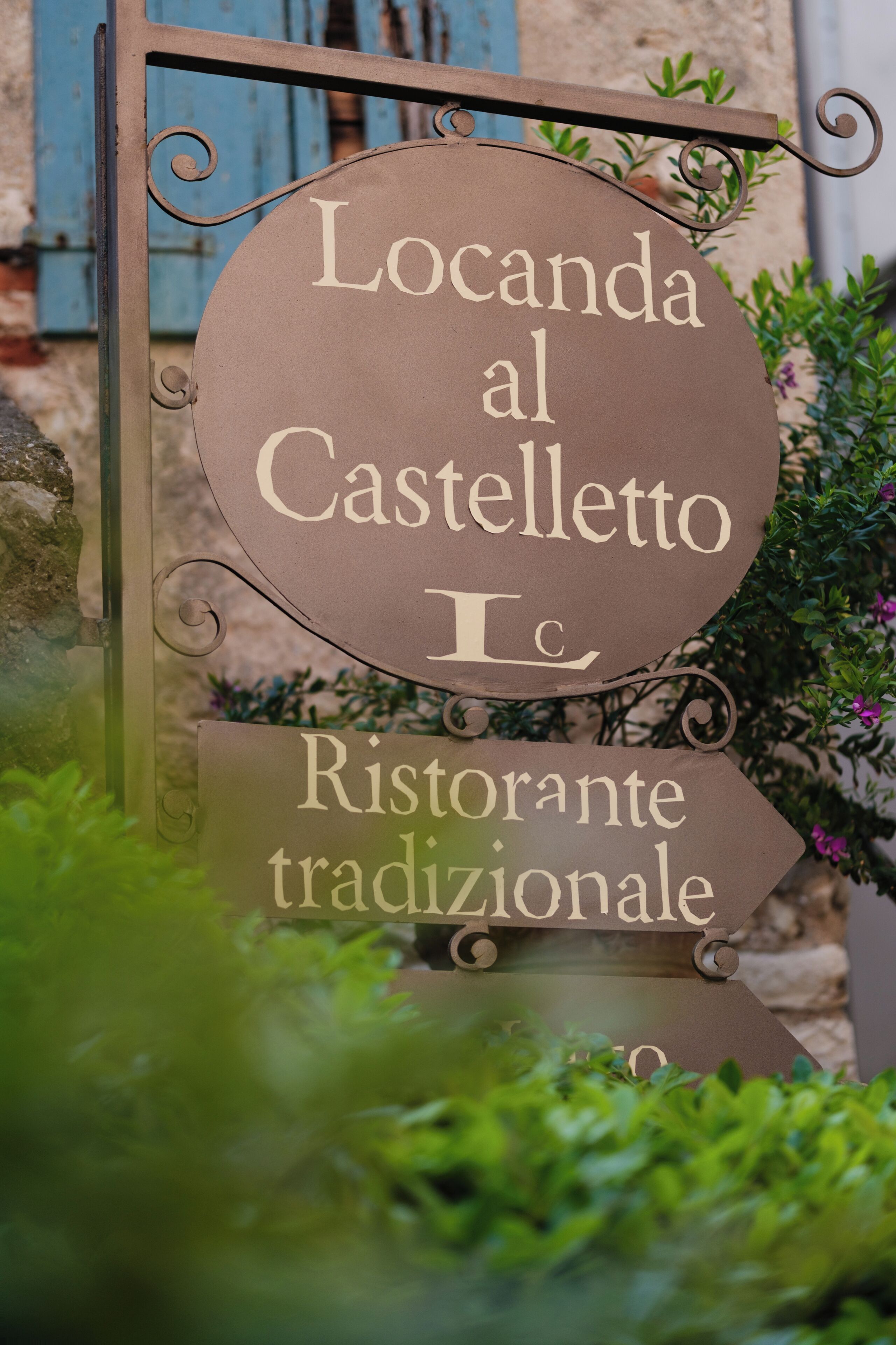 A sign for 'Locanda al Castello Ristorante tradizionale' with a rustic metal frame and decorative swirls.