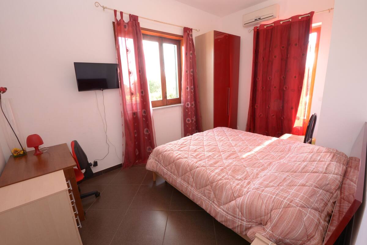 Une chambre à coucher avec un lit, un bureau, une chaise, un téléviseur et une fenêtre avec des rideaux.