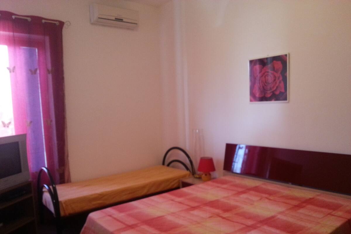 Une chambre avec deux lits, un bureau, une chaise, une télévision et un climatiseur fixé au mur.