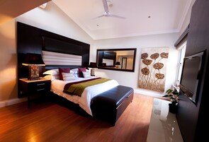 A modern bedroom with a large bed, a nightstand with a lamp, a ceiling fan, a large mirror, and a wall with a floral design.