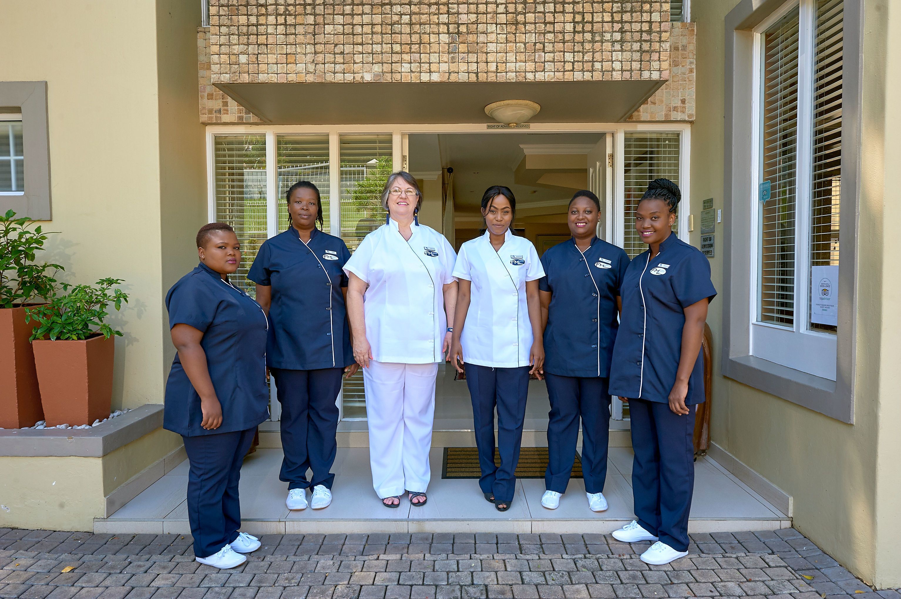 A group of people standing in front of a building with a tiled entrance and a potted plant to the left.