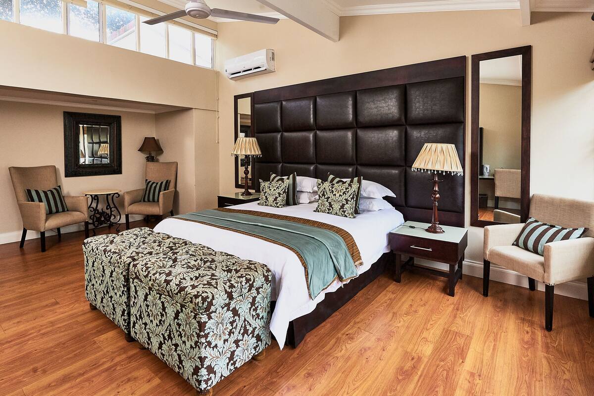 A spacious hotel room with a large bed, two armchairs, a side table, and a mirror.
