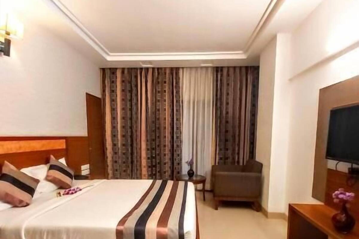Una habitación de hotel con cama, una silla, una mesita y televisor.