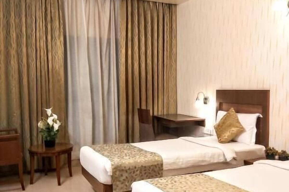 Habitación de hotel con dos camas, un escritorio, una silla y una mesita con un florero.