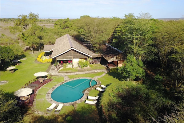 A house with a swimming pool, surrounded by lush greenery and a deck with lounge chairs.