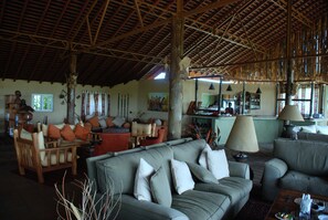 A spacious living area with a high wooden ceiling, a sofa set, and a dining table.